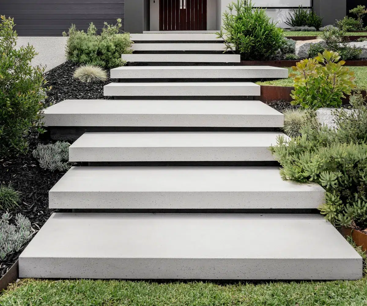 Concrete steps with black trim leading through a landscaped garden with shrubs and mulch