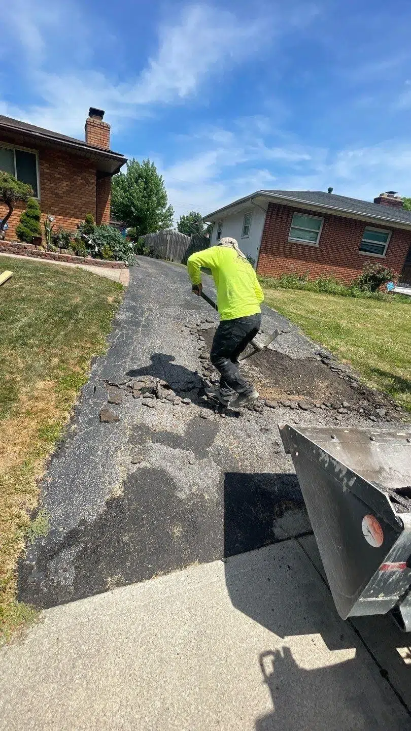 Worker removing broken asphalt during residential driveway demolition before replacement